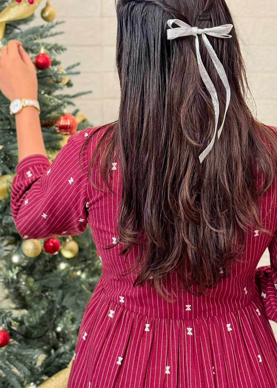 Person wearing a red dress with white patterns, standing in front of a decorated Christmas tree.