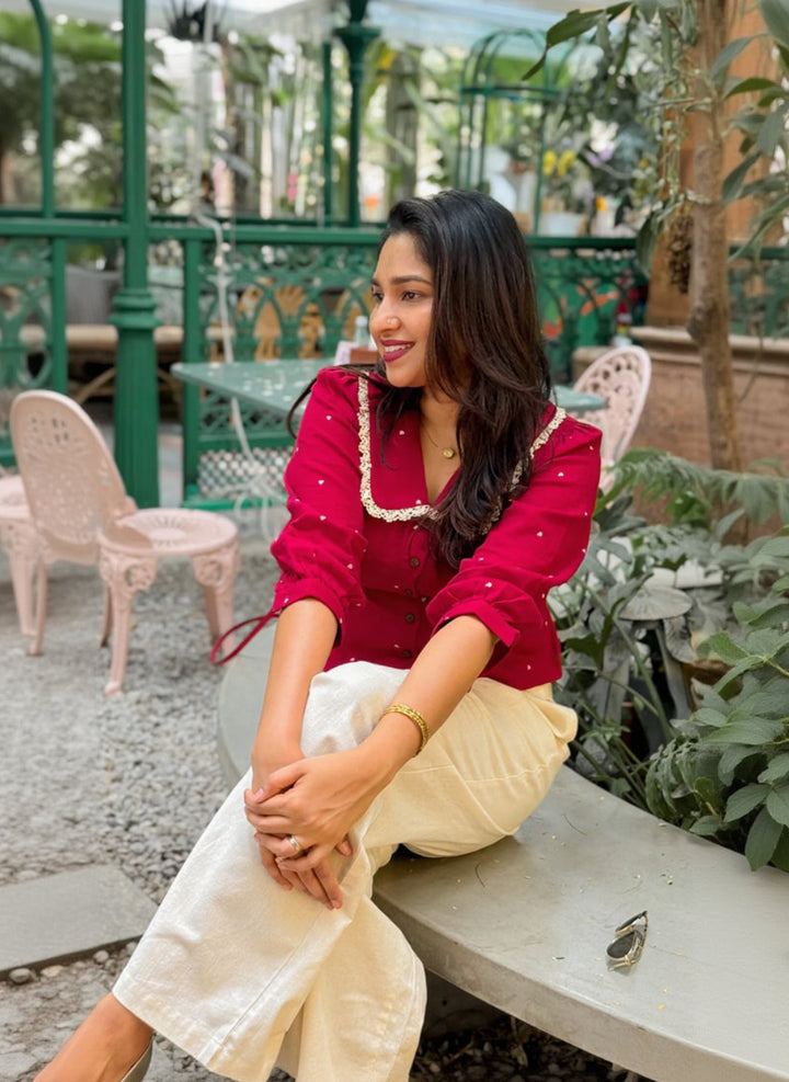 Woman in a red top and white pants sitting on a bench outdoors.